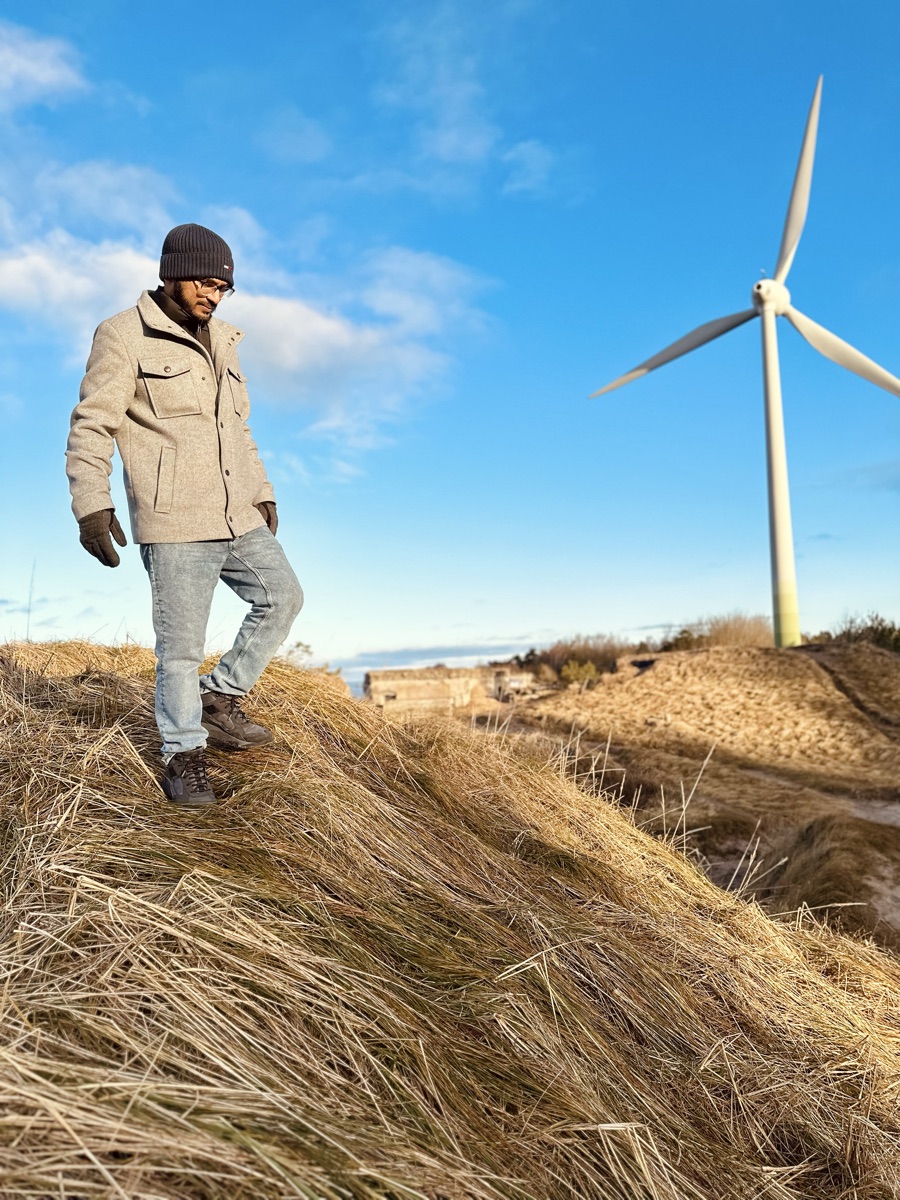 A lone figure walking a coastal path toward wind turbines